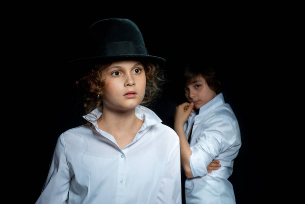 preteen boy and girl in white shirts and hat posing in studio on dark background - Photo, Image