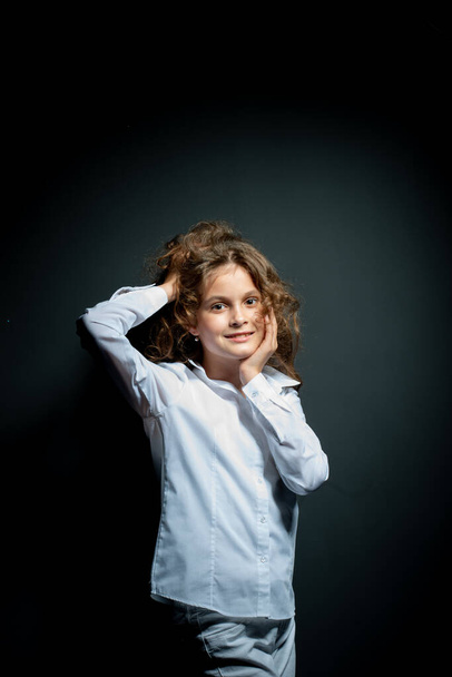 adorable preteen girl in white shirt posing on dark background and looking at camera - Φωτογραφία, εικόνα