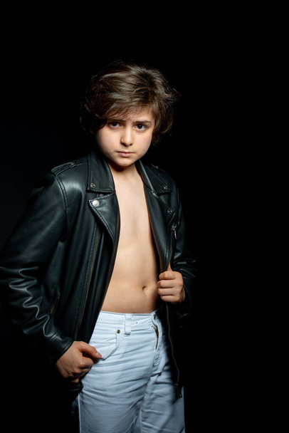preteen boy in black leather jacket posing on black background - Фото, изображение