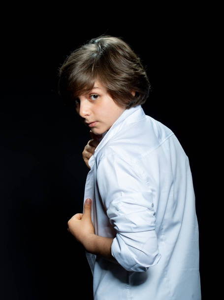 preteen boy in white shirt posing on black background and looking at camera - Foto, imagen