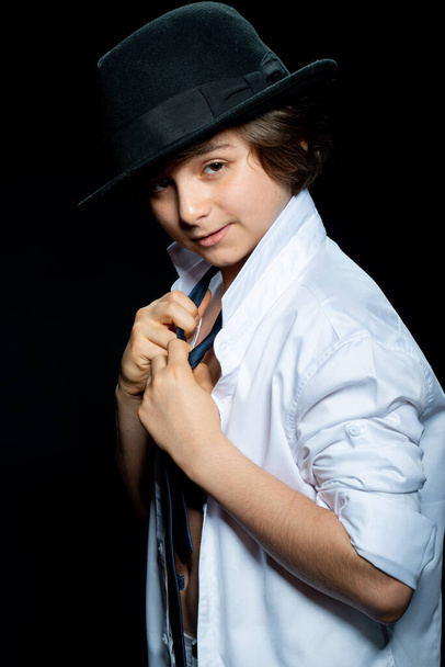 preteen boy in white shirt and hat posing on black background - 写真・画像
