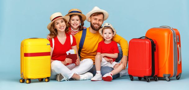 Cuerpo completo feliz padres e hijos con equipaje, pasaportes y billetes sonriendo y mirando a la cámara contra el backdro azul
 - Foto, Imagen