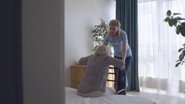 Volunteer girl helping old lady with walking frame, support for disabled seniors - Felvétel, videó