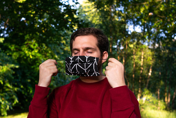 Foto de un hombre joven y atractivo en el parque que pone una máscara facial reutilizable
  - Foto, Imagen
