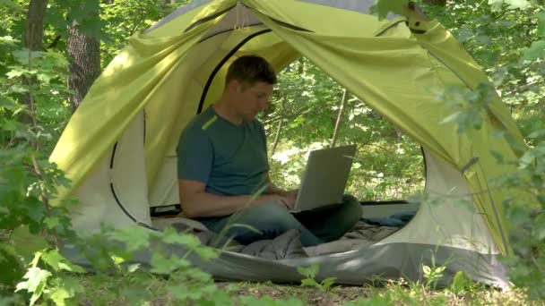 Geschäftsmann arbeitet hinter einem Laptopin in einem Zelt im Wald - Filmmaterial, Video