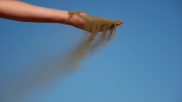Αργή άμμος που χύνεται από το χέρι μιας γυναίκας με ένα φωτεινό γαλάζιο ουρανό πίσω - Πλάνα, βίντεο