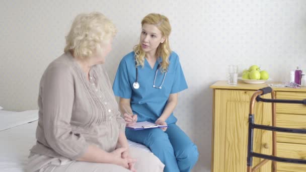 Female doctor talking to elderly patient writing prescription papers, healthcare - Metraje, vídeo