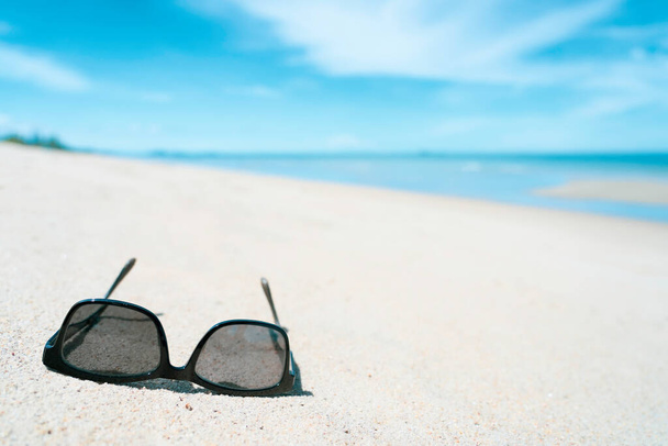 Oculos de sol na praia de areia branca com mar de cor turquesa no verão horário ensolarado
 - Foto, Imagem