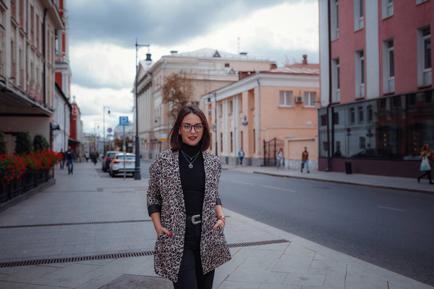 Beautiful young brunette woman walks in Moscow. In a trendy leopard jacket. Smiling and walking on the city. Going shopping. - Φωτογραφία, εικόνα