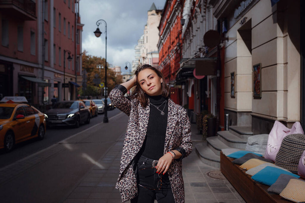 Krásná mladá brunetka chodí po Moskvě. V módní leopardí bundě. Usmívat se a chodit po městě. Jedeme nakupovat. - Fotografie, Obrázek