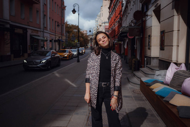 Hermosa joven morena camina en Moscú. Con una chaqueta de leopardo de moda. Sonriendo y caminando por la ciudad. Ir de compras
. - Foto, Imagen