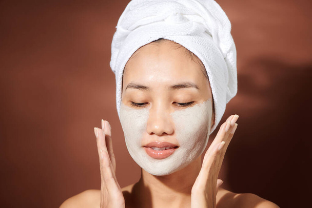 Jovem mulher asiática aplicando máscara de barro em seu rosto
.  - Foto, Imagem