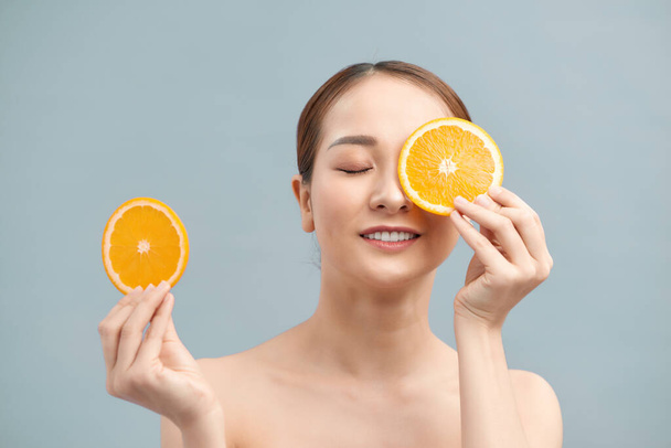 Świetne jedzenie dla zdrowego stylu życia. Piękna młoda kobieta bez koszuli trzyma kawałek pomarańczy przed okiem stojąc na białym tle - Zdjęcie, obraz