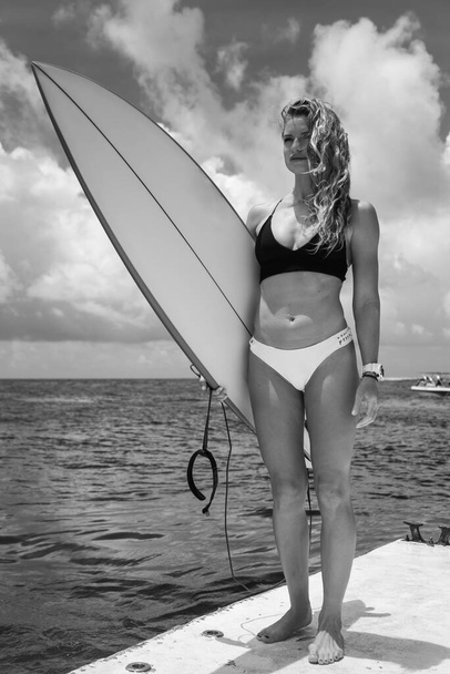 Black and white portrait of young blonde woman in bikini with surfboards on background, she is smiling - Valokuva, kuva