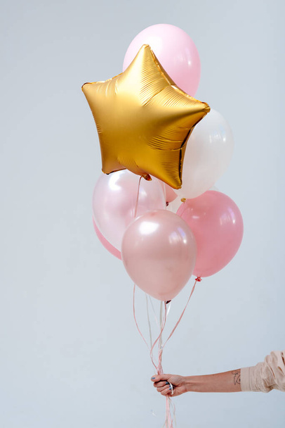 Composition of white, pink, transparent helium balloons and gold star in the hand of a woman on a white background. - Φωτογραφία, εικόνα