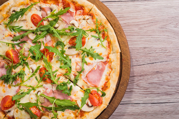 Tuore pizza prosciutto-lihalla, tomaatilla ja vihreällä arugulalla puupöydällä. ylhäältä - Valokuva, kuva