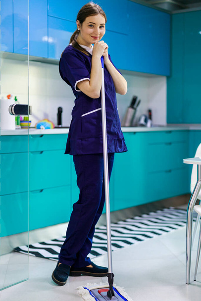 Mujer joven limpiando el suelo de baldosas con fregona en la cocina
. - Foto, Imagen