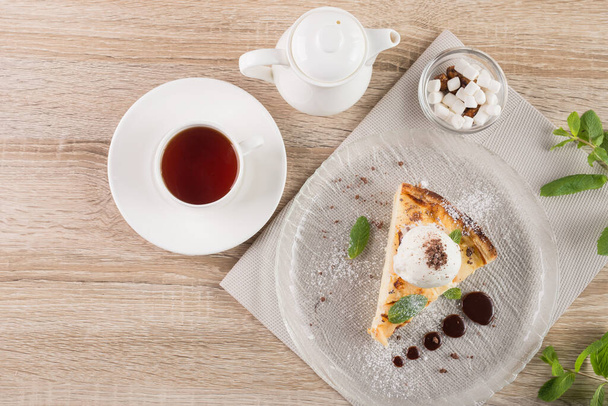 Νόστιμο κέικ με φύλλα δυόσμου και μπάλες παγωτού, λευκό φλιτζάνι τσάι σε ένα ξύλινο τραπέζι. Γλυκό φόντο επιδόρπιο. Άνω όψη. - Φωτογραφία, εικόνα