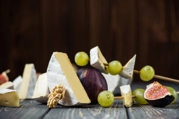 egy darab camembert vagy brie sajt szőlővel, fügével és dióval egy fa asztalon. csemegék borral - Fotó, kép
