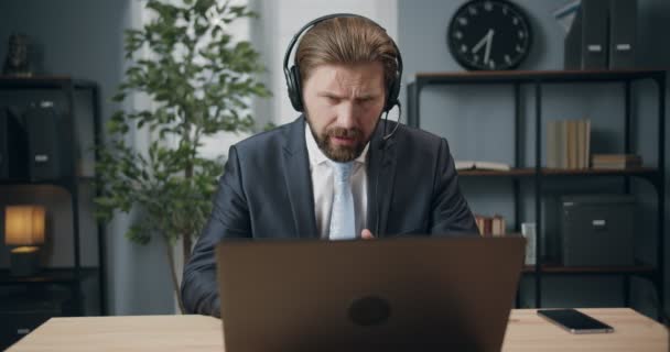 Przystojny mężczyzna w garniturze i słuchawkach rozmawiający z klientem - Materiał filmowy, wideo