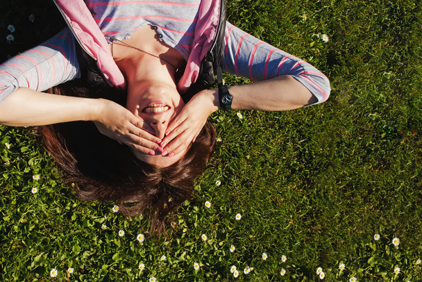 Young smiling woman lying on the grass with small daisy flowers, - Foto, afbeelding