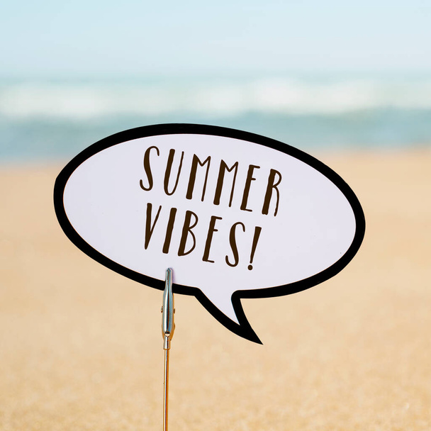 Nahaufnahme eines Sprechballons mit dem Text Sommerstimmung, der am Sand eines ruhigen Strandes klebt, mit dem Meer im Hintergrund - Foto, Bild