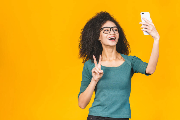 młody zabawny Afryki casual lady grymaszenie i co selfie na smartfon odizolowany na żółtym tle. - Zdjęcie, obraz