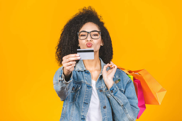 Shopping Concept - Portrait young beautiful african american woman smiling and joyful with colorful shopping bags and credit card isolated over yellow Background. Copy Space. - Foto, Imagem