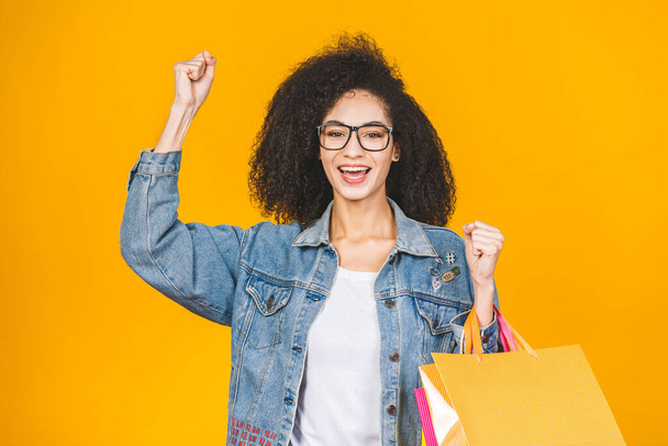Alışveriş Konsepti - Portre güzel Afro-Amerikan kadın gülümseyen ve renkli alışveriş torbalarıyla dolu sarı Pastel duvar arkasında izole edilmiş. Boşluğu Kopyala. - Fotoğraf, Görsel