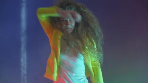 Uma mulher engraçada em uma jaqueta amarela pula e dança energeticamente na luz do néon e fumaça
 - Filmagem, Vídeo