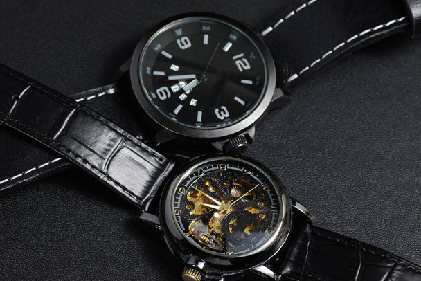 a black automatic self winding wristwatch with transparent sekeleton dial design and a black battery operated watch on black leather background - Photo, Image