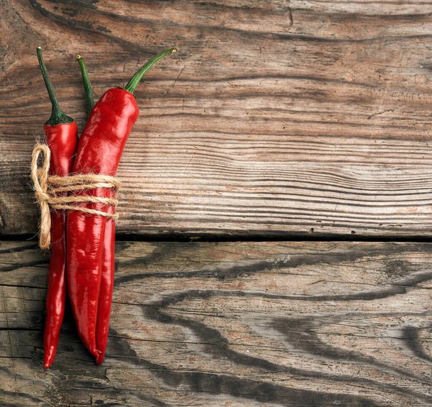 pods of red chili peppers tied with a brown rope on a gray wooden background, top view, copy space - Foto, immagini