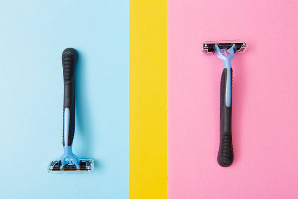2 hojas de afeitar desechables azules, una enfrente de la otra sobre un fondo azul y una en rosa. Para hombres y mujeres
 - Foto, imagen