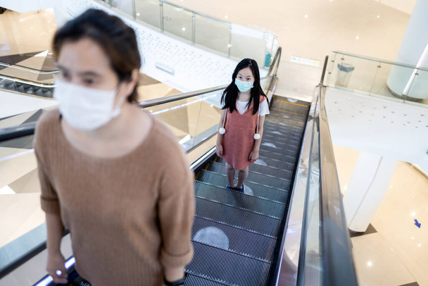 Οι άνθρωποι, φορώντας προστατευτικές μάσκες προσώπου, χρησιμοποιώντας κυλιόμενες σκάλες κρατώντας την απόσταση στο σύμβολο των λευκών κύκλων στις κυλιόμενες σκάλες, ασφάλεια, κοινωνική απόσταση στο εμπορικό κέντρο κατά την επαναλειτουργία του, νέα κανονική ζωή - Φωτογραφία, εικόνα