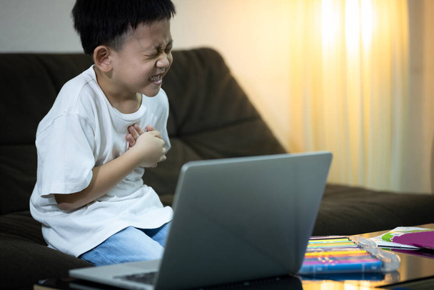 Aziatisch kind jongen met pijn op de borst lijden aan een hartaanval, klein kind man met moeite met ademhalen, pijnlijk, symptomen van hartproblemen of aangeboren hart-en vaatziekten tijdens het studeren online thuis - Foto, afbeelding