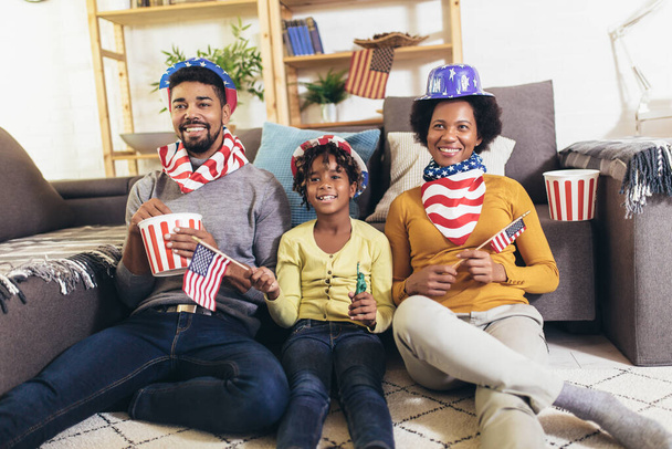 Happy African American perhe kolme katsomassa televisiota ja hurraavat urheilupelit sohvalla kotona
 - Valokuva, kuva