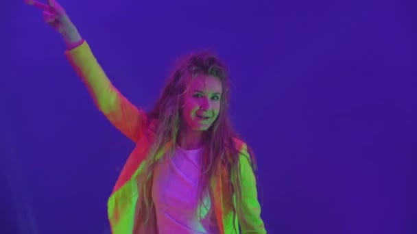 Nainen tanssii iloisesti ja katsoo kameraa strobovalojen ja valonheittimien valossa. Neon värit ja hullu tyttö tanssia musiikkia ja laulua - Materiaali, video
