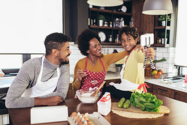 Happy black family spending day at kitchen. Girl using phone. - Fotó, kép