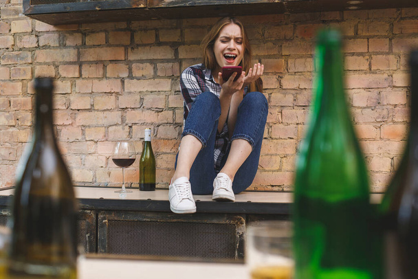 Junge Frau mit Alkoholproblemen sitzt mit geschlossenen Augen in Küche. Depressive junge weibliche Teenager, die Problemgefühle wie Leiden und Weinen missbraucht haben. Telefonieren.  - Foto, Bild