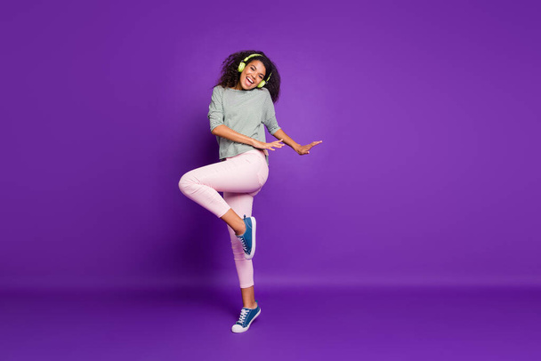 Full length photo of crazy funky brunette hair teen afro american girl have break pause listen song use headset dance dancer wear striped shirt blue pink sneakers isolated violet color background - Φωτογραφία, εικόνα