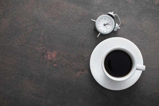 Cup of coffee with alarm clock on table, office break concept, vintage concrete background - Fotó, kép
