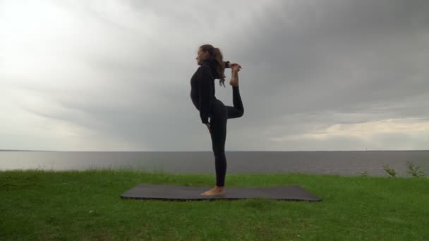Junge, fitte Frauen praktizieren Yoga an der Küste in der Nähe des Sees oder Meeres. Frau macht Herr des Tanzes Natarajasana Pose - Filmmaterial, Video