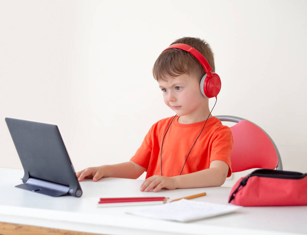 Δυσκολίες μάθησης παιδιών σε απευθείας σύνδεση. Ένα παιδί που δεν καταλαβαίνει έναν δάσκαλο συνεδρίων που κοιτάζει την ταμπλέτα. Φοράει ακουστικά. Διαδικτυακή μάθηση. E-μελέτη στο σπίτι - Φωτογραφία, εικόνα