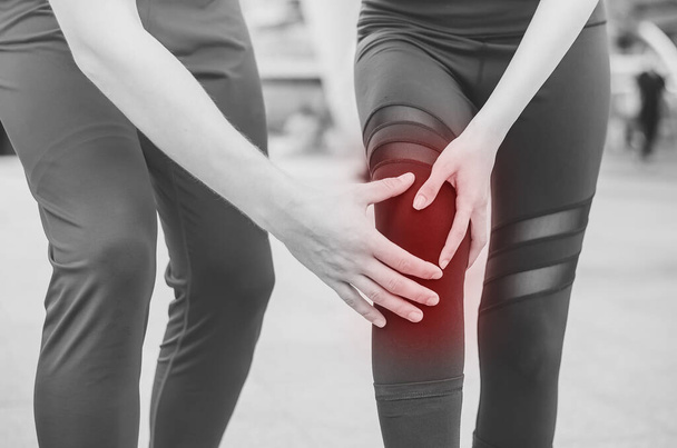 Чорно-білий тон, гомілковостопний тренажер, який допомагає бігун у болю. Жінка-спортсменка, яка зазнала аварії під час марафону, з болючою ногою на колінах допомагають особистий тренер або медик
. - Фото, зображення
