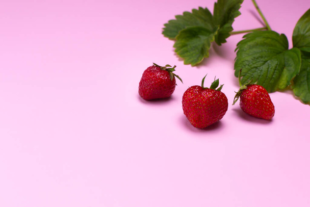 Ripe strawberries and green leaves on a pink background. Copy space. Horizontal orientation. - Foto, imagen