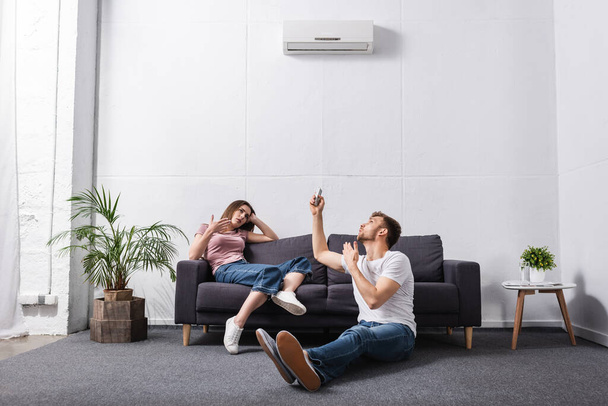 sad couple with remote controller at home with broken air conditioner  - Foto, imagen