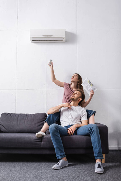 pareja agotada con mando a distancia y periódico que sufre de calor mientras está sentado en casa con el aire acondicionado roto
  - Foto, Imagen