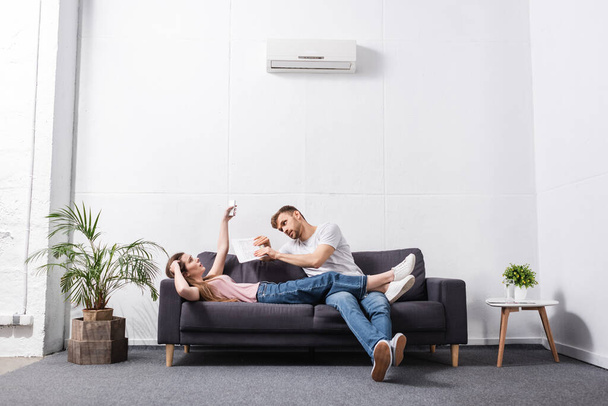 sad young couple with remote controller suffering from heat at home with broken air conditioner  - Фото, зображення