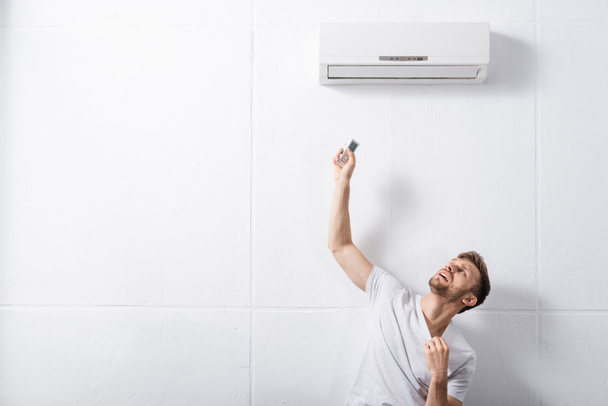 hombre confundido sosteniendo mando a distancia y sufriendo de calor con el aire acondicionado roto en casa
  - Foto, Imagen