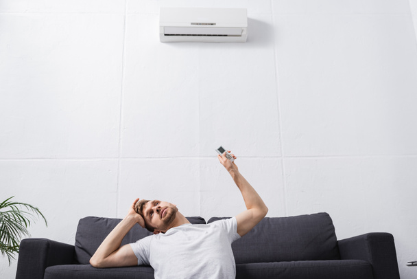 frustrado hombre sosteniendo mando a distancia y sufriendo de calor con el aire acondicionado roto en casa
  - Foto, Imagen